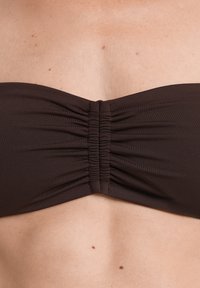 Rjav bikinijski zgornji del brez naramnic s pripomočkom z nabranim materialom na sredini. Narejen iz gladkega materiala, ponuja brezšivno, minimalistično zasnovo.