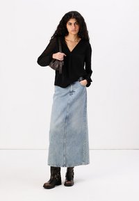 Svart bluse med delvis gjennomsiktige, mønstrede ermer, sammen med et langt, lyseblått denimbukse skjørt og svarte, hæl ankle boots med metallisk dekor.