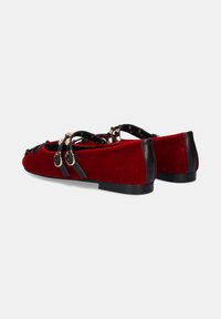 Bailarinas de ante rojo con detalles en cuero negro, con puntera redondeada y correa decorativa con herrajes dorados. Suela plana para mayor comodidad.