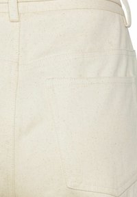 Krämfärgade jeans med en strukturerad yta, synliga sömmar och en bakficka med kvadratiska hörn.