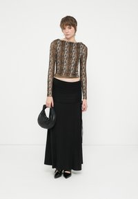 Top cropped de manga longa castanho com design de padrão animal, combinado com uma saia maxi preta com franzidos. A modelo segura uma carteira curva preta.