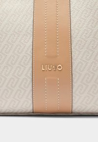 Sac à main en cuir blanc avec une sangle d'accent beige clair ornée de coutures embossées et un logo "LIUJO" doré. Motif de fond texturé.