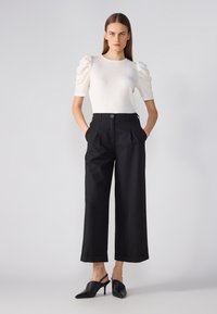 Top alb cu nervuri, cu mâneci bufante, asortat cu pantaloni largi negri, cu talie înaltă. Pantofii cu toc slingback negri completează ținuta.