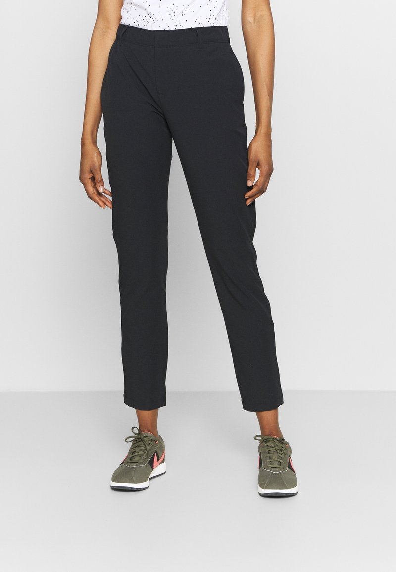 Svarta, smalare byxor med en slät yta och elastisk midja. I kombination med grå sneakers med rosa detaljer.