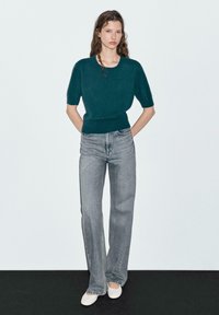 Türkisfarbener Strickpullover mit kurzen Ärmeln, kombiniert mit hellgrauen, weit geschnittenen Jeans und weißen flachen Schuhen. Einfaches, klares Design mit lockerer Passform.