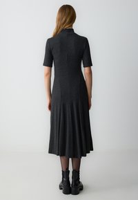 Koolgrijze jersey jurk met korte mouwen, een uitlopende rok en een hoge kraag. Gekleed met zwarte enkellaarsjes en sheer panty’s.