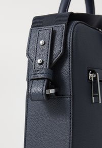 Marine farvet tekstureret lædertaske med en robust rem med sølv hardware og en lynlåslomme. Glat finish og struktureret design.
