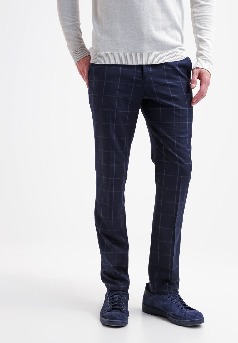 Marinblå rutig byxor i mjukt tyg, med slim fit och ett subtilt rutmönster samt sidofickor. Matchas med blå sneakers.