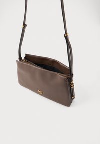Hnědá kožená crossbody taška s nastavitelným popruhem, zlatým kováním a částečně otevřenou hlavní kapsou se zipem na bílém pozadí.