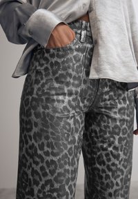 Pantalons en imprimé léopard gris avec une texture brillante, dotés d'un bouton à la taille et de poches latérales, associés à une chemise en satin gris clair.