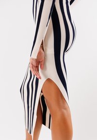Abito a righe a coste in blu navy e crema, con maniche lunghe e spacco laterale, che mette in risalto il tessuto testurizzato e il design aderente.