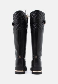 Czarne kozaki za kolano z pikowanym cholewkami, z bocznym zamkiem błyskawicznym, ozdobione złotym paskiem na obcasie i zaokrąglonym przodem.