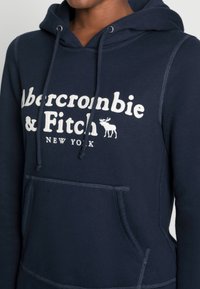 Sudadera con capucha de color azul marino con el logotipo blanco de "Abercrombie & Fitch", bolsillo tipo canguro y capucha con cordón; suave y de tejido de algodón texturizado.