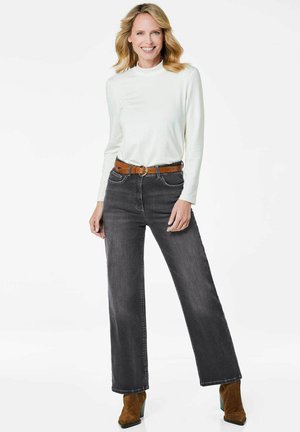 Jeans gris à jambes larges avec poches avant, associés à un haut à manches longues blanc et une ceinture marron. Des bottines marron complètent la tenue.