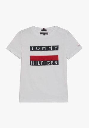 Hvid T-shirt med korte ærmer med et sort, hvidt og rødt rektangulært logo med teksten "Tommy Hilfiger" foran.