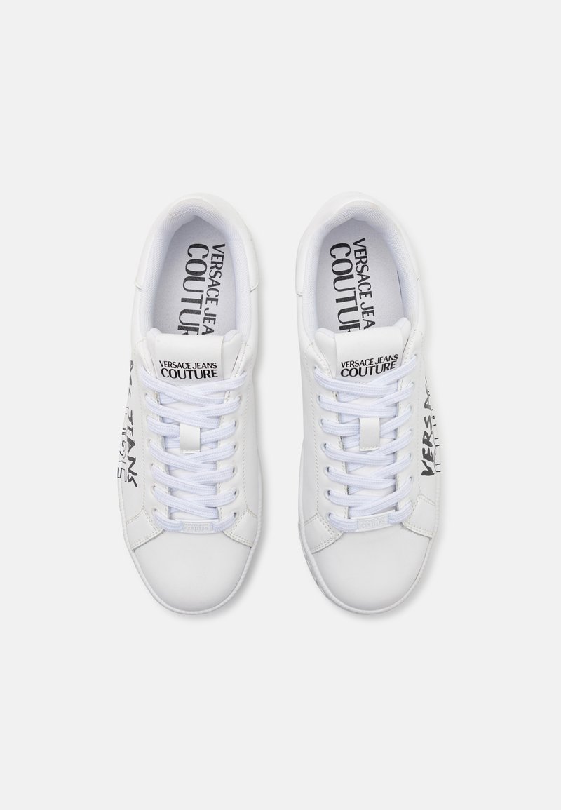 Zapatillas blancas con un exterior de cuero liso, cordones blancos planos y una marca negra prominente en los lados y la lengüeta.