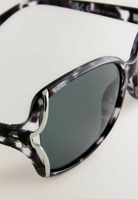 Occhiali da sole a motivo nero e grigio con una montatura spessa, dettagli in argento e lenti scure, che mostrano elementi di design moderni e curvi.