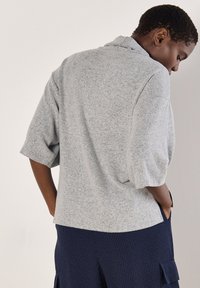 Helles graues, übergroßes, kurzärmliges Sweatshirt; weiche Textur mit lockerer Passform und subtilen Sprenkelmustern, kombiniert mit dunkelblauen, gestreiften Hosen.