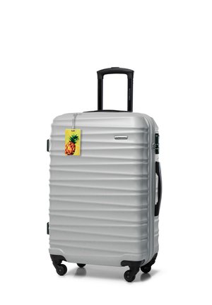 Silver hard-shell suitcase with four wheels, black retractable handle, side handles, and a yellow pineapple luggage tag attached.