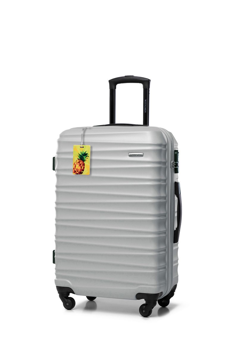 Silver hard-shell suitcase with four wheels, black retractable handle, side handles, and a yellow pineapple luggage tag attached.