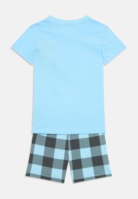 Camiseta de manga corta azul claro combinada con pantalones cortos a cuadros en negro y azul claro, exhibida sobre un fondo blanco.