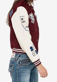 Maronowa kurtka varsity z białymi rękawami, z niebieskimi haftami i naszywkami, w tym rokiem "2021" oraz szczegółami w kształcie konturów stanu.