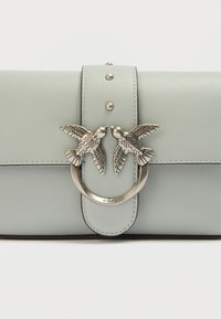 Τσάντα χειρός από δέρμα ανοιχτού πράσινου χρώματος με λεία υφή, που διαθέτει κυκλικό κλείσιμο από ασημένιο μέταλλο διακοσμημένο με δύο μοτίβα πουλιών.
