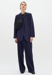 Námořnický oversize blazer s velkým knoflíkem, spárovaný se širokými námořnickými kalhotami. Černá crossbody taška se zipem a texturované kožené boty.