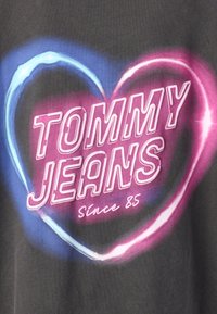 Maglietta grigia grafica con design a forma di cuore con accenti neon rosa e blu. Il testo recita "TOMMY JEANS" e "Dal 85".