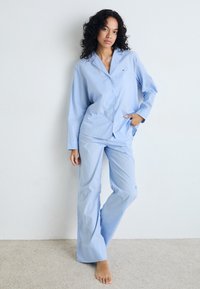 Ljusblå randig pyjamasset i mjukt tyg, med en skjorta med knappar och bröstficka samt löst sittande byxor.