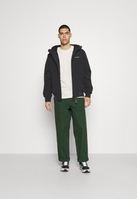 Veste noire à capuche, t-shirt blanc, pantalon cargo vert et baskets noires. Design simple, coupe décontractée et détails minimalistes.