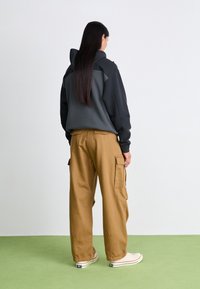 Gray hoodie with a fitted hood, paired with loose brown cargo pants featuring side pockets. The background is a soft green.