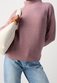 Light pink ribbed knit sweater with a high collar, paired with light blue denim jeans and a white shoulder bag. Textured fabric detail visible.