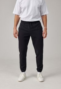 Zwarte katoenen sweatpants met een elastische tailleband, taps toelopende benen en zijzakken, gecombineerd met een wit T-shirt en witte sneakers.