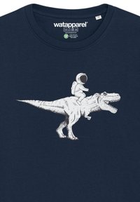 T-shirt en coton bleu marine avec un graphique blanc représentant un astronaute chevauchant un T-rex, détaillé avec des textures et des lignes.