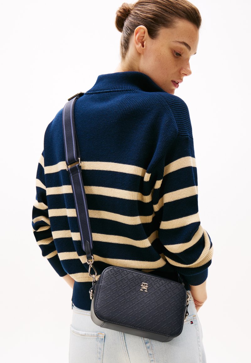 Maglione a righe blu e crema abbinato a una borsa a tracolla blu scuro con un design testurizzato e accessori in oro.
