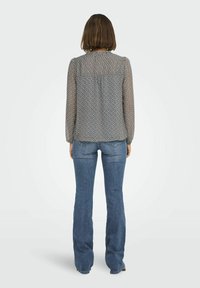 Blouse fluide à motifs avec des manches longues dans des tons de bleu et de beige, assortie à un jean bleu évasé. La vue arrière met en avant le design et l'ajustement.