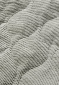 Quilted fabric in light gray with textured, rounded patterns and vertical stripes; soft, plush surface displaying subtle color variation.