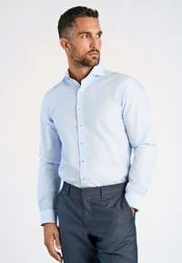 Lichtblauw, knoopsluitend overhemd met een gestructureerde kraag, lange mouwen en een subtiele textuur, gecombineerd met donkergrijze broek.