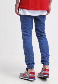 Blå denim-joggers med elastiska muddar, ihop med grå och röda sneakers. Joggersarna har en klassisk skärning med bakfickor och lätt blekning.