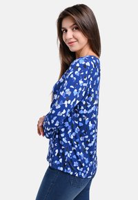 Langärmliges Hemd mit blauem Muster, das abstrakte Formen in Hellblau, Dunkelblau, Schwarz und Weiß zeigt. Weicher Stoff mit lockerer Passform.