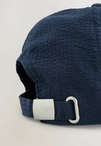 Gorra de color azul marino con tejido texturizado, que presenta una hebilla de metal plateado en la parte trasera y una visera curvada. El material es suave y ligero.