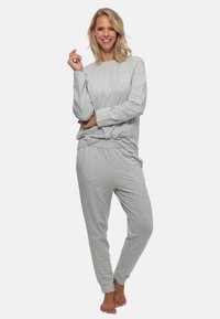 Lysegrå loungewear sæt indeholder en langærmet top og matchende bukser. Stoffet virker blødt med en afslappet pasform og elastisk talje.