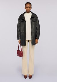 Giacca di pelle nera con due tasche sul petto, maglione di beige chiaro, pantaloni a zampa di elefante color crema, borsa color bordeaux e scarpe con tacco marroni.