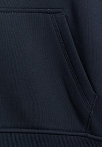 Gros plan d'une poche en tissu bleu marine foncé avec des coutures visibles sur un vêtement, montrant clairement la texture et les coutures.