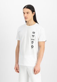 Tricou alb din bumbac cu desene grafice negre, inclusiv un semn de pace, cuvântul "LIBERTATE" și forme abstracte, cu mâneci scurte.