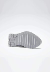 Grå yttersula på en Reebok-sneaker med en texturerad yta, horisontella spår och en tydlig logga på hälen.