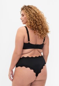 Bralette nera con pizzo e mutande a vita alta. Tessuto liscio con bordi ondulati, spalline regolabili e chiusura a gancio sul retro.