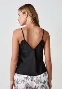 Camisole en satin noir avec des détails délicats en dentelle au niveau des bretelles, dotée d'un dos en V, d'une texture lisse et d'une coupe décontractée.