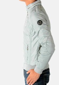 Lysegrå dunjakke med tætsiddende design, ribstrikkede manchetter, lynlåslommer og quiltet tekstur på skuldrene. Sølvfarvede metaldele.